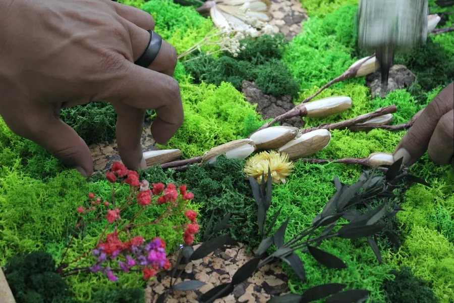 Hands setting dried flowers and stems into a bed of moss